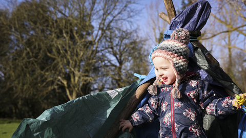 Child wrapped in warm clothing in front of tarp shelter
