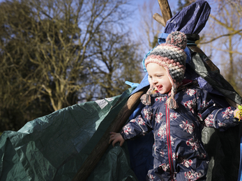 Child wrapped in warm clothing in front of tarp shelter