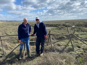 Two volunteers standing in front of new fence at Two Tree Island