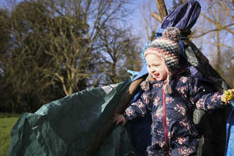 Child wrapped in warm clothing in front of tarp shelter