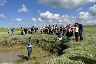 Students getting a demonstration of how to take a sample of saltmarsh mud
