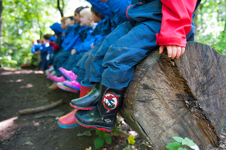 A line of children sat on a tree trunk wearing wellies, spiderman ones at the forefront