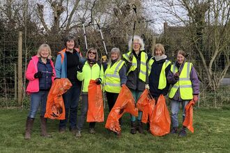 Sue Huggett and Littlebury Green Group with litterpickers in the air and bags ready to collect rubbish
