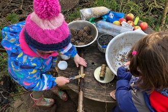 Children playing outside at a table with natural objects.