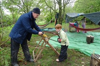 Volunteer and boy sawing a piece of tree together.