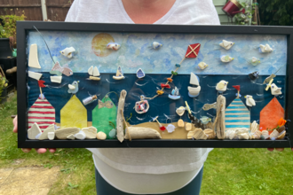 Beverley holding up 3D artwork of a beach scene with litter and other beach-combed objects incorporated.