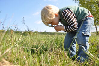 Boy looking through magnifying glass in meadow
