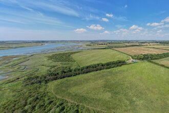 Aerial image of the fields at Abbotts Hall with a blue sky and saltmarsh with meandering water creeks in the distance.