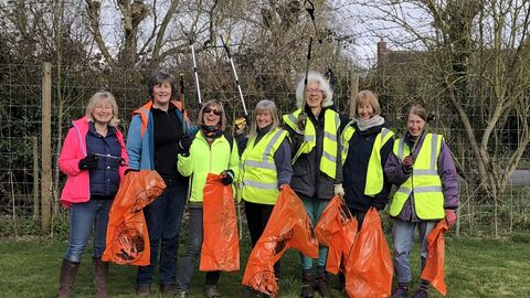 Sue Huggett and Littlebury Green Group with litterpickers in the air and bags ready to collect rubbish