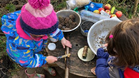 Children playing outside at a table with natural objects.