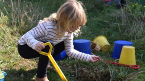 child digging in grass and mud