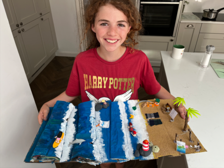 A young girl holds up a 3D artwork scene of a beach and ocean.