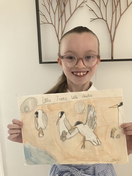 A young girl holds up winning drawing of seabirds on the beach.