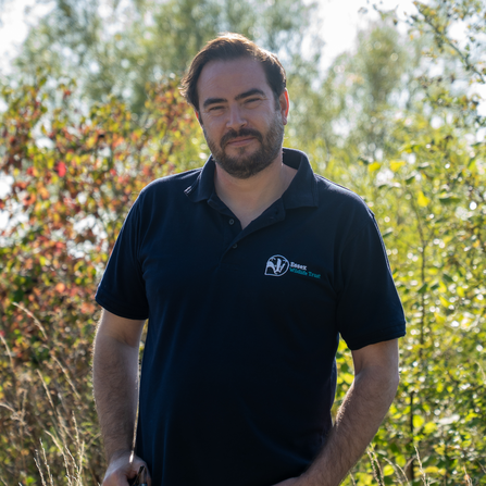 Man stood in front of trees with Essex Wildlife Trust logo uniform