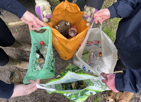 Picture of 4 people holding bags open filled with litter collected. 
